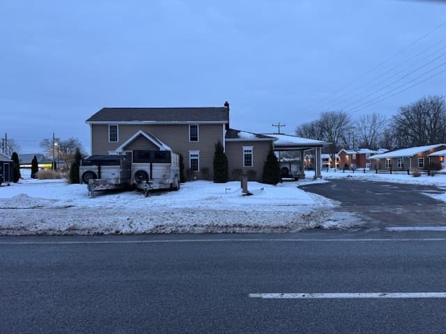 Two-story gray house with restoration vehicle parked in snowy driveway